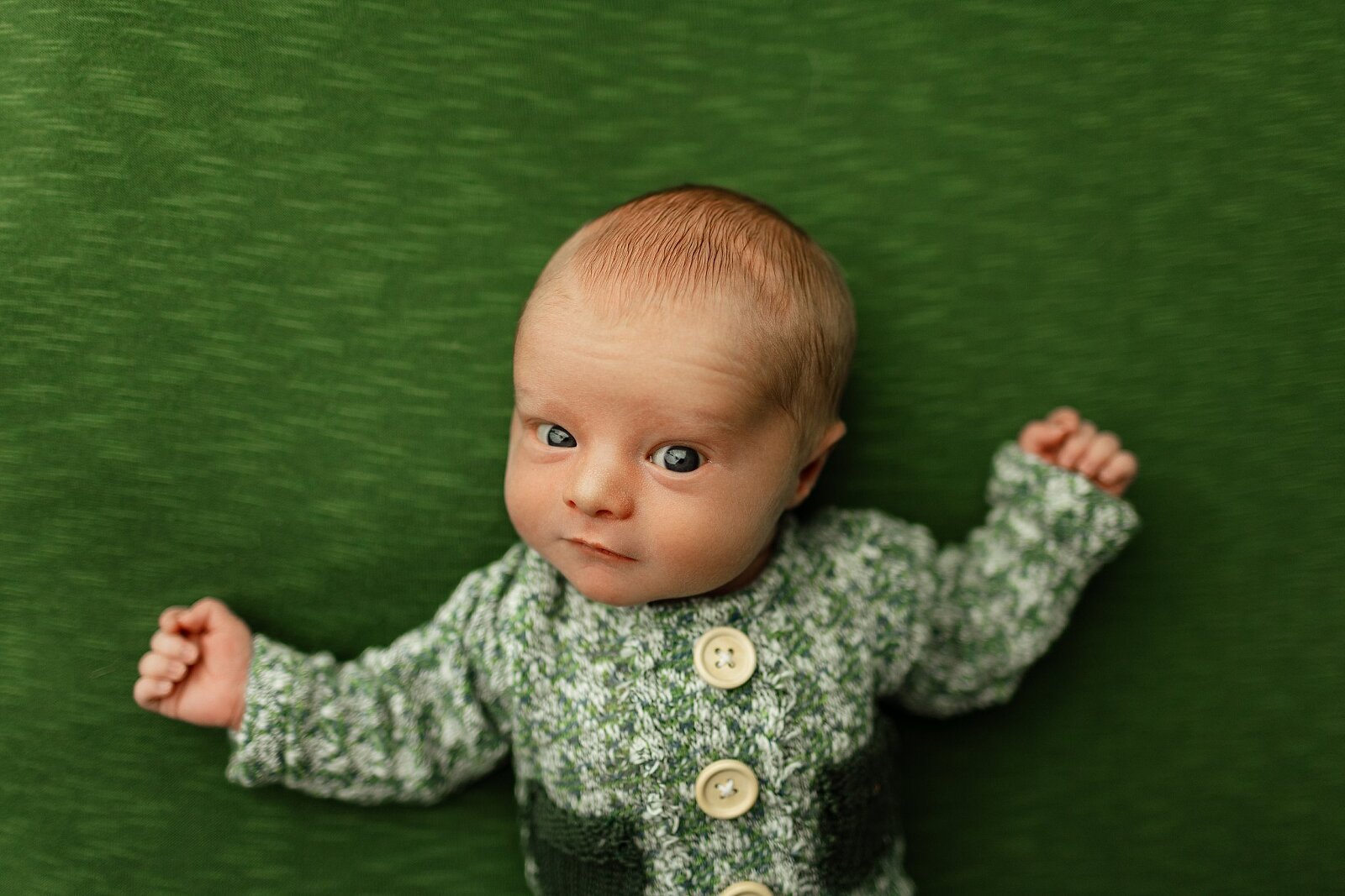 baby wearing green and white checkered newborn outfit on a green backdrop